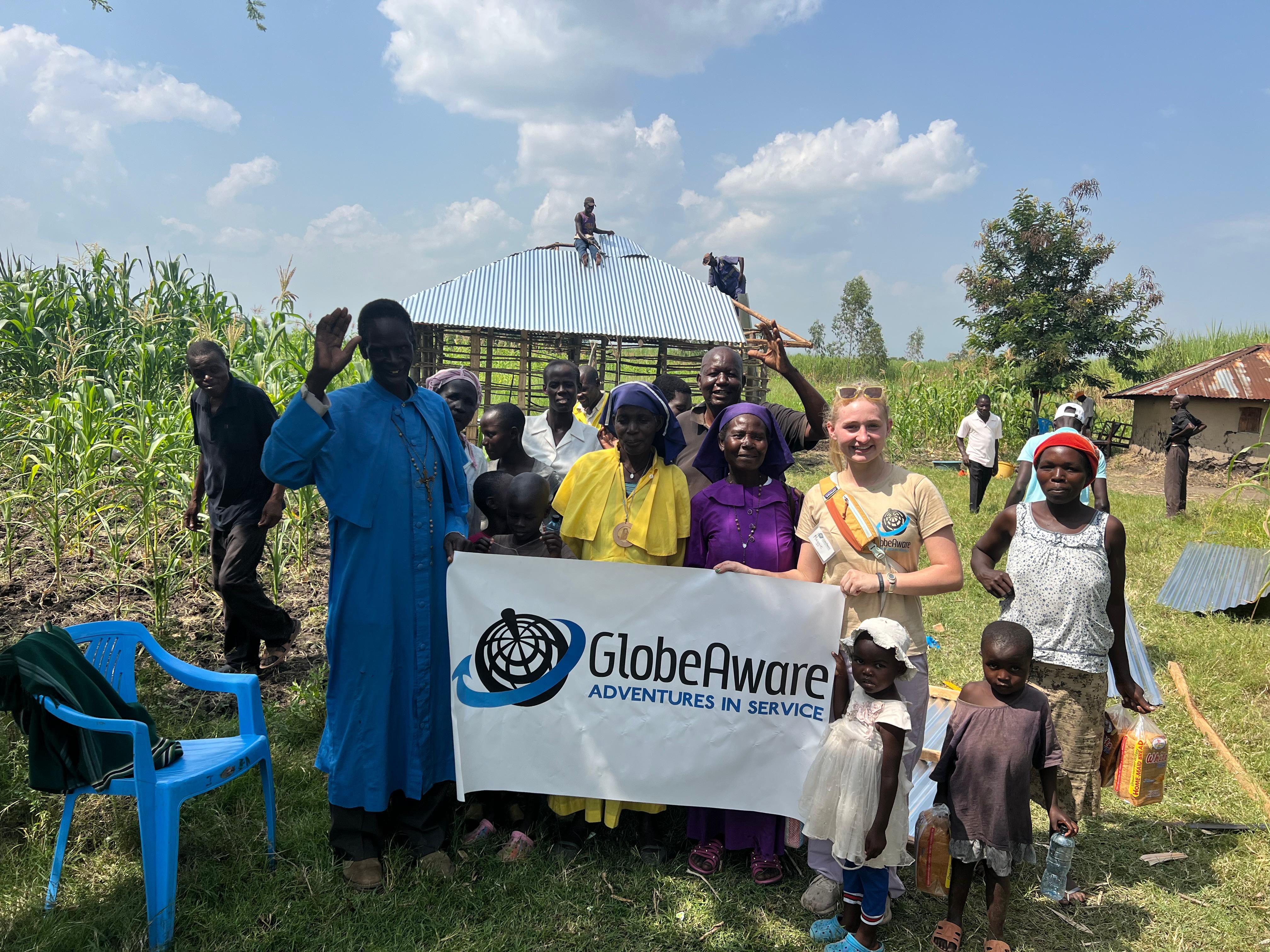 Team of volunteers and local residents in Kisumu, Kenya, standing together with a GlobeAware banner in front of a house under construction